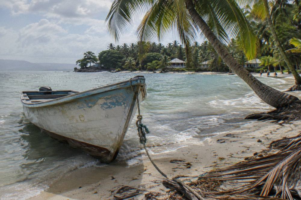 A wooden boat moored beside a palm-lined white sand beach on a small island