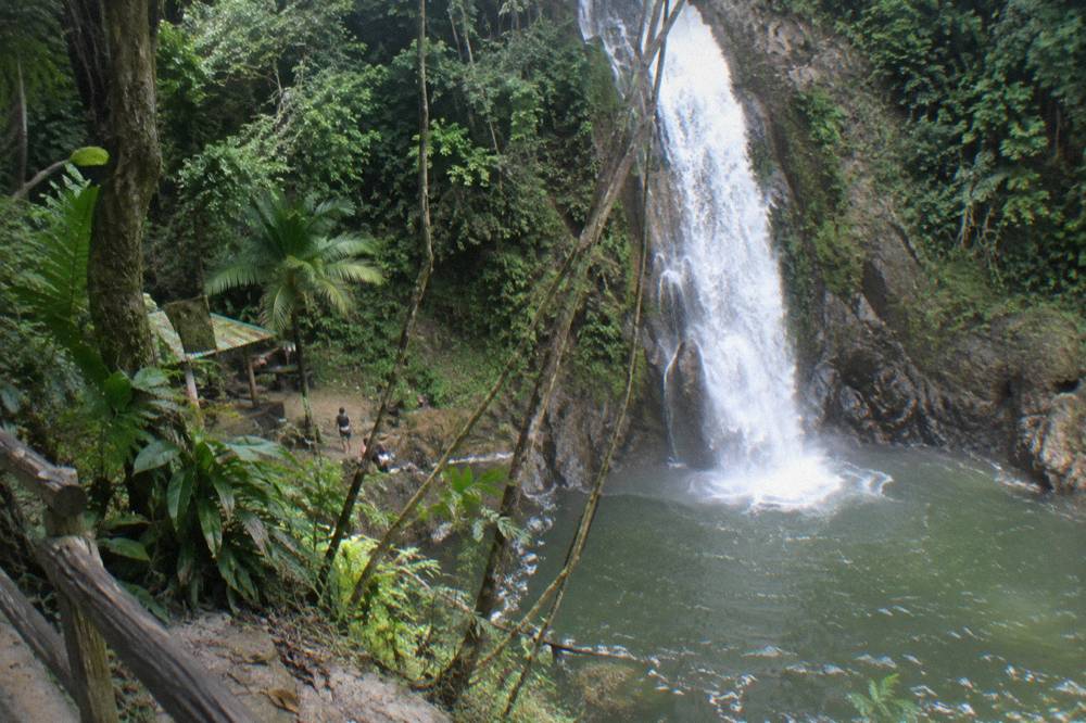 Wide view of a tall white waterfall dropping down a rock face into a dark green pool