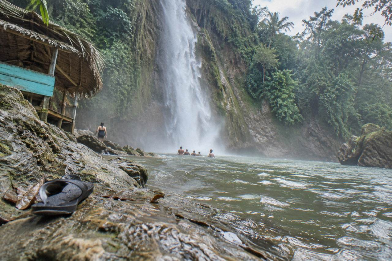 Tall jungle waterfall pouring into a natural pool surrounded by dense green hills