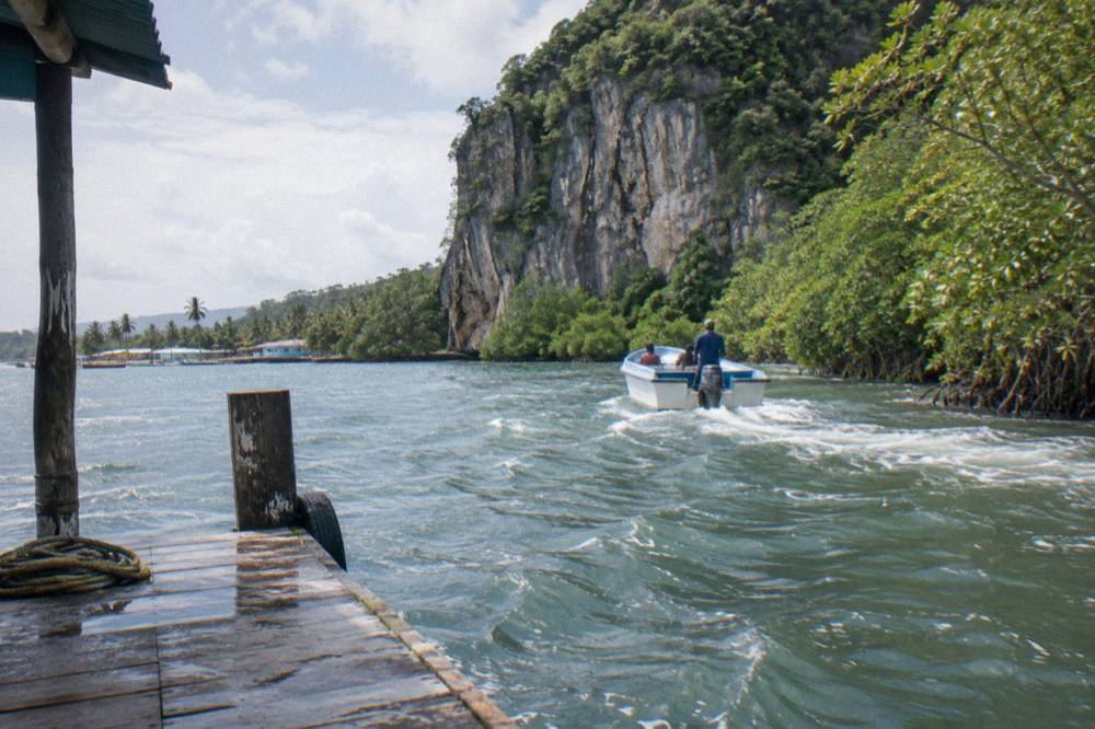 Small open boat cruising a narrow mangrove channel toward a limestone cliff