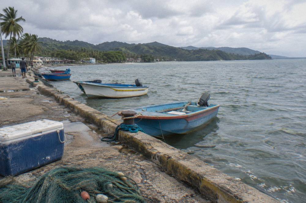 Small town waterfront with fishing boats moored along a seawall under a pale morning sky