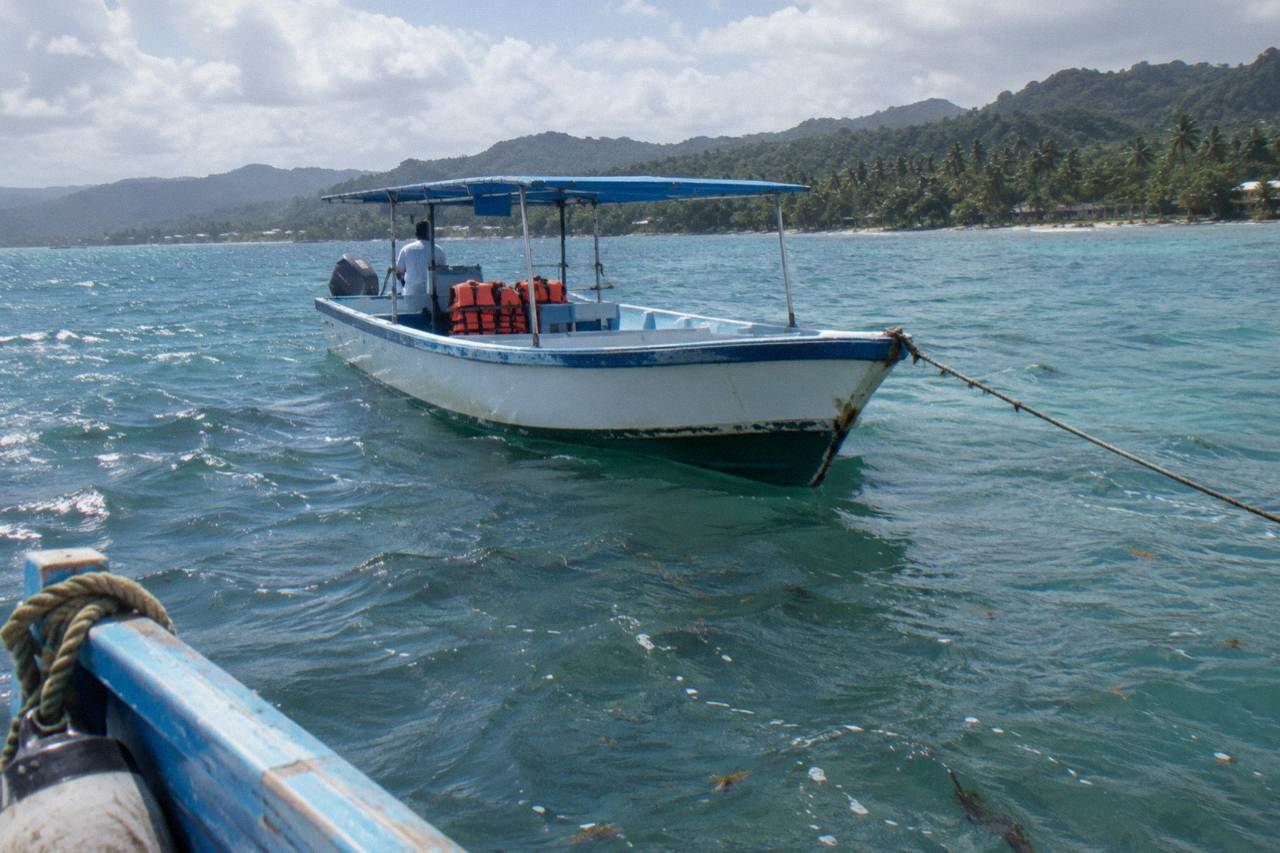 Calm turquoise water of Samaná Bay with a small passenger boat at anchor under a morning sky