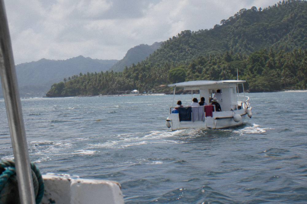 Small tour boat crossing a calm tropical bay toward forested hills