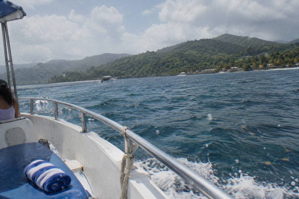 A whale watching boat cruising across a wide blue bay toward forested hills