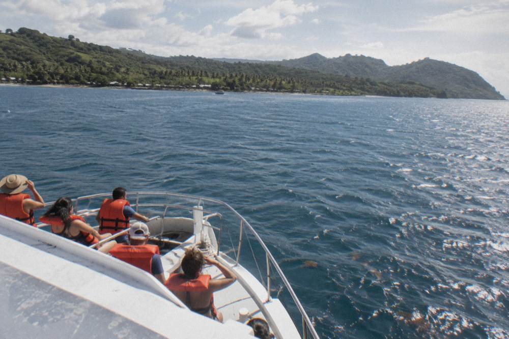 A tour boat with passengers in orange life jackets crossing Samaná Bay