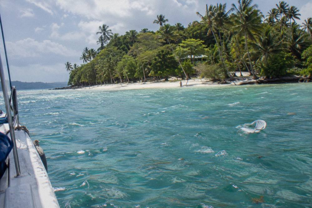 A tour boat anchored beside a small tree covered Caribbean island with pale sand and clear shallow water.