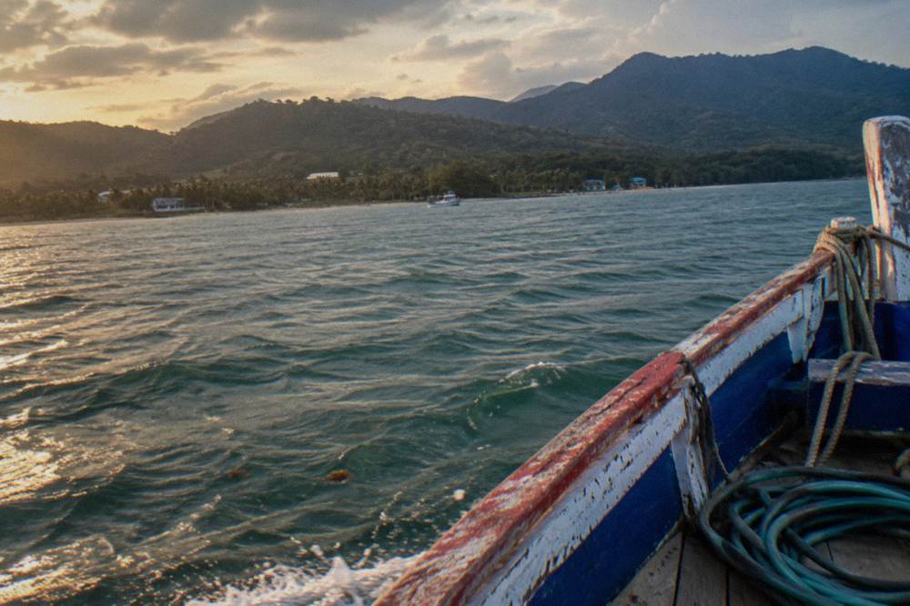 A wooden whale watching boat cruising across a calm bay toward green hills in the distance.