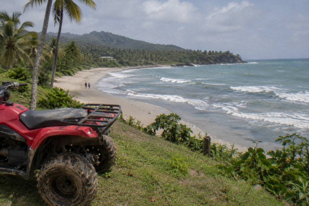 An all-terrain vehicle parked on grass above a wide empty beach with rolling surf