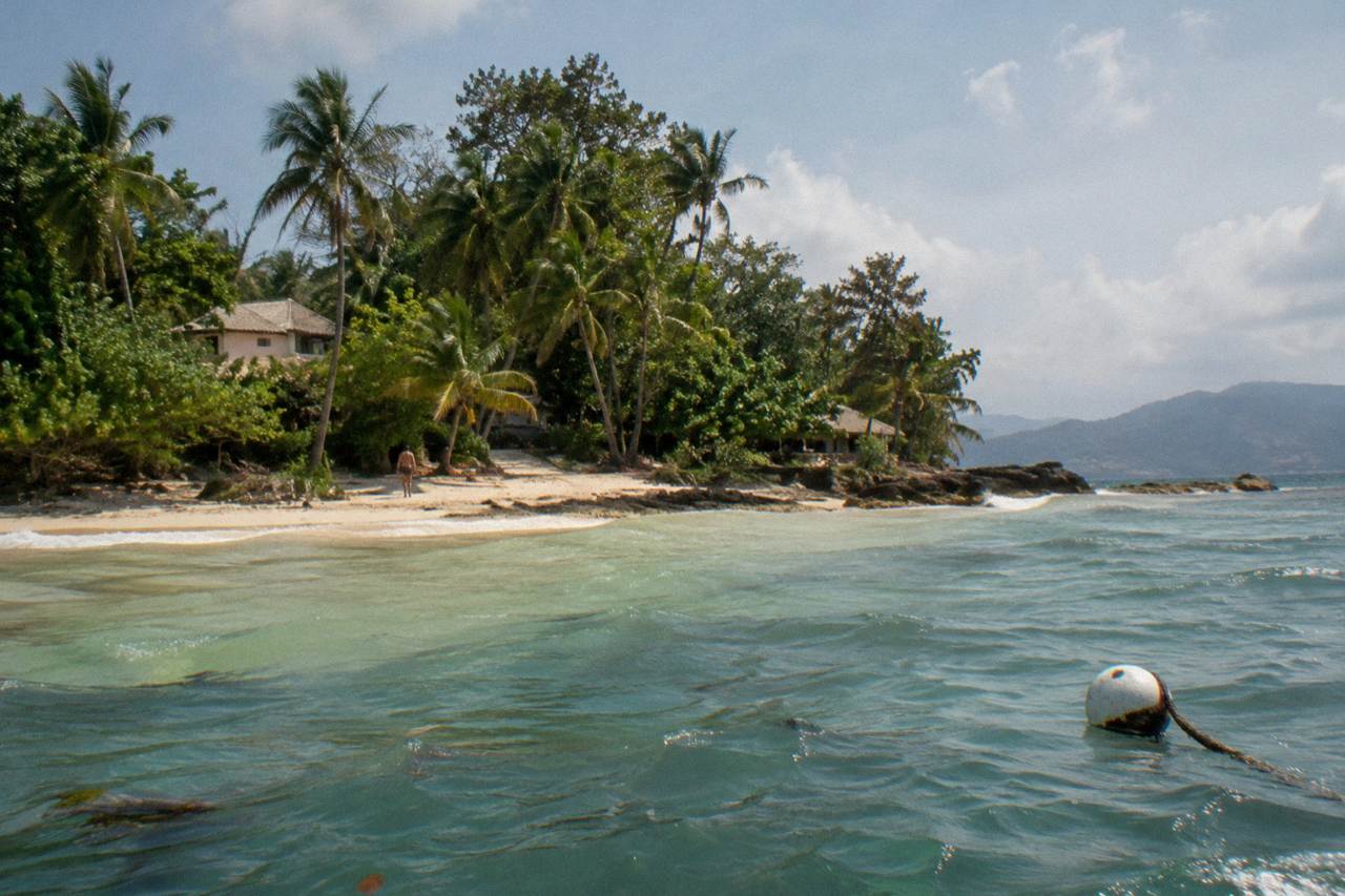 A small wooded island with a pale sand beach sitting in calm Caribbean water near Samana