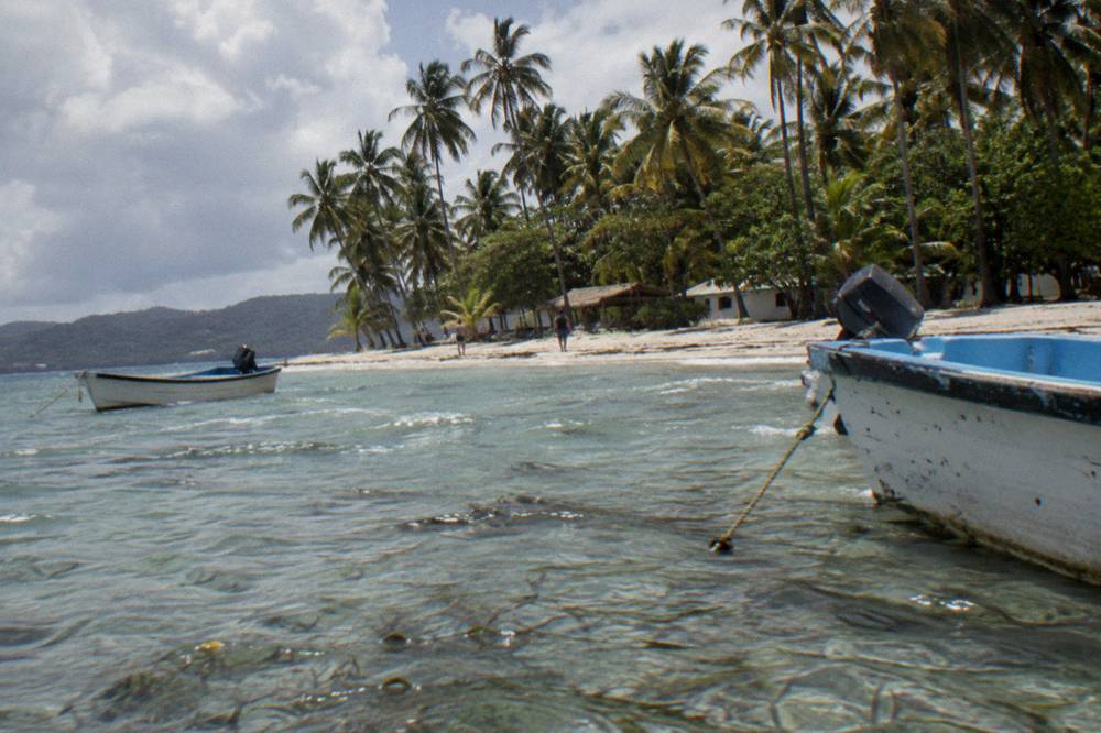 A palm-lined island beach with a shallow sandbar and moored small boats