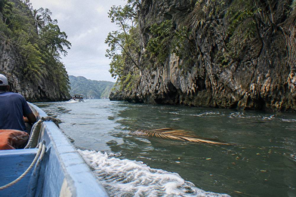 A small open boat cruising through a narrow mangrove channel with limestone cliffs on both sides