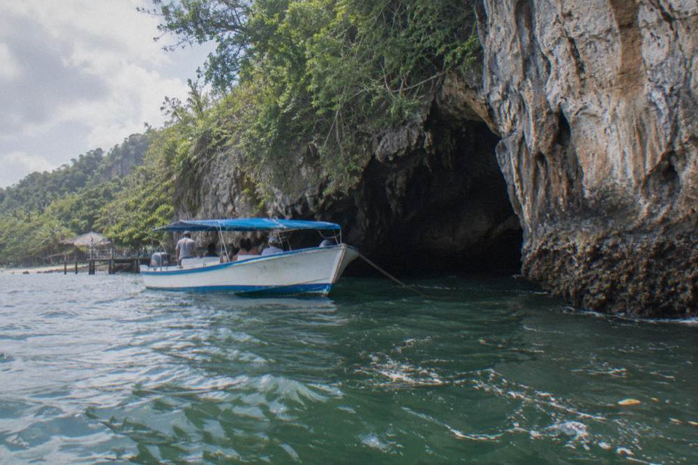 A tour boat anchored beside a limestone cliff face at the entrance of a sea cave