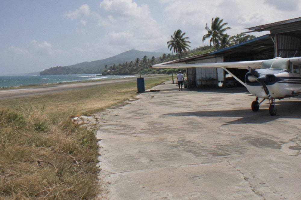 Regional airport apron with a single turboprop aircraft parked beside a low terminal and green hills
