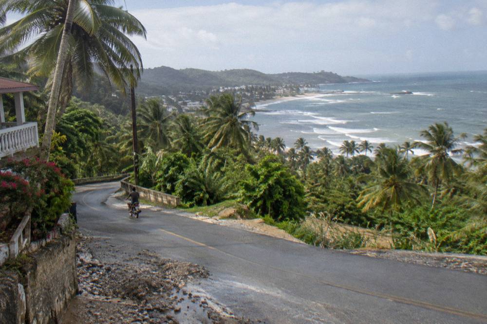 Winding two-lane road through green palm-covered hills with distant coastline visible