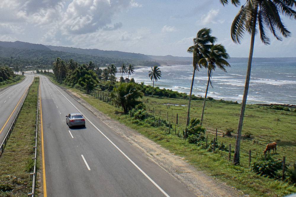 Toll highway curving through green farmland with a car in the right lane
