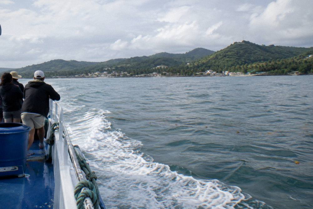 A whale watching boat with passengers on deck moving across a wide calm bay