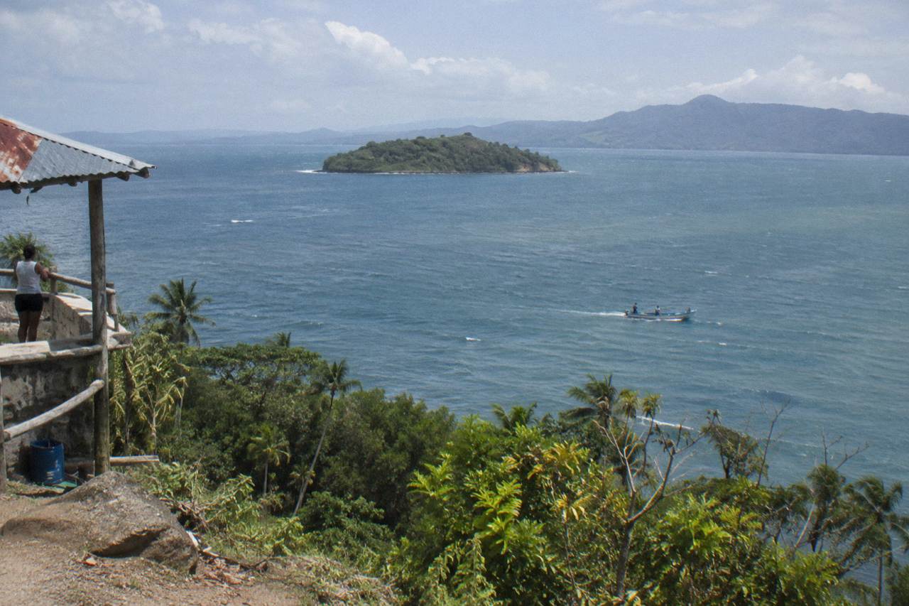 A calm wide bay with green hills rising behind a small island and open water