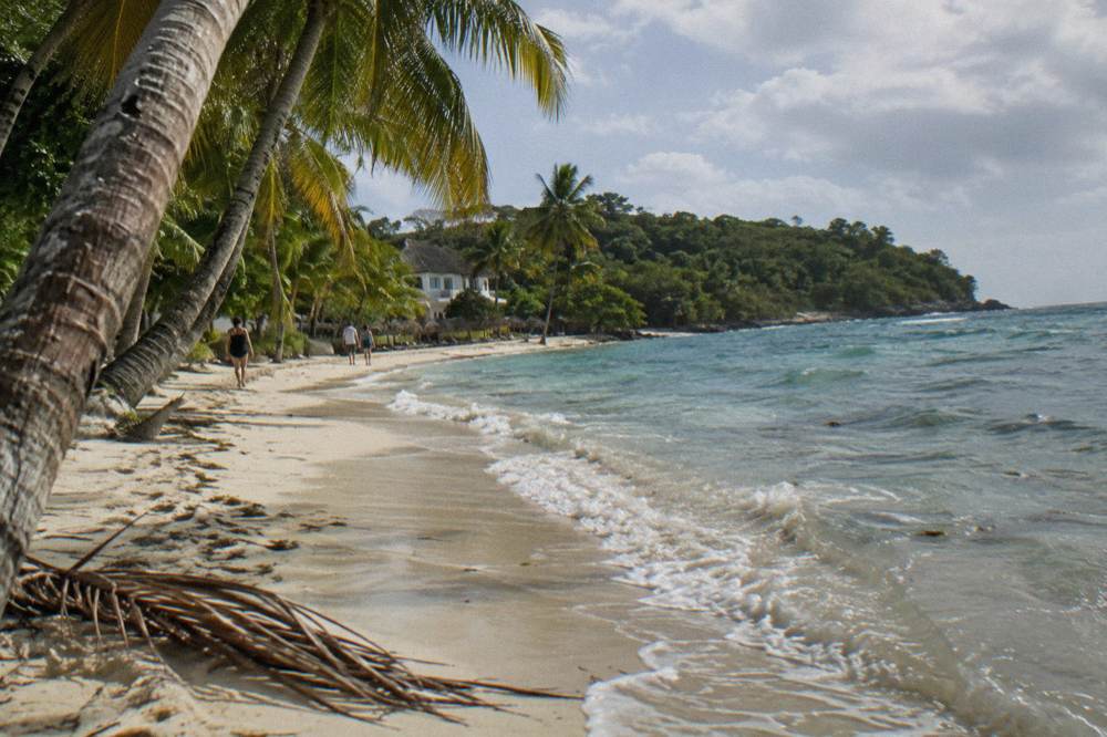 An empty beach with white sand, leaning palms and clear shallow water.