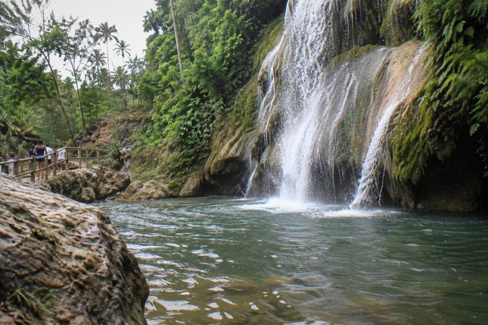 Water pouring over a mossy rock ledge into a dark plunge pool at the base of a waterfall