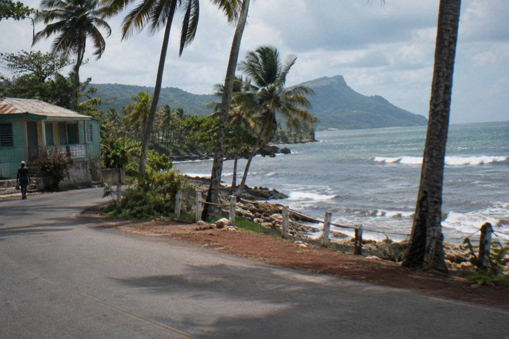 Open tour bus on a coastal road with palm trees heading toward Samana Bay