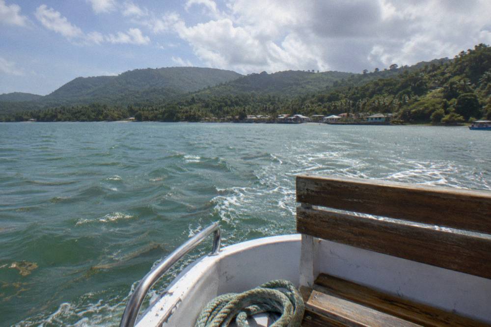 Open tour boat crossing a wide calm bay toward forested hills