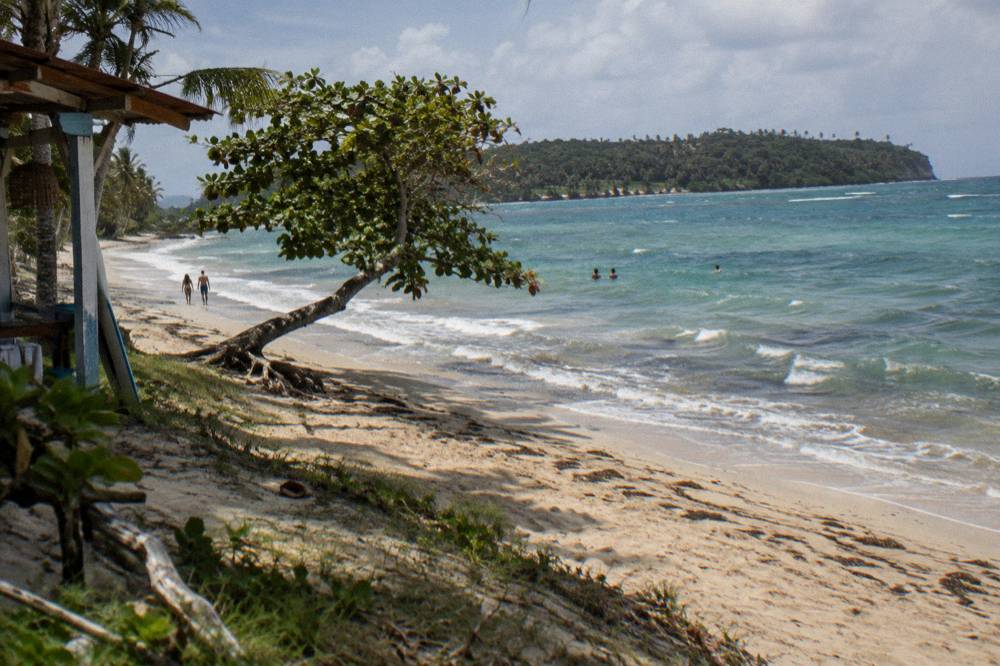 Wide sandy beach with turquoise shallows and a wooded island on the horizon