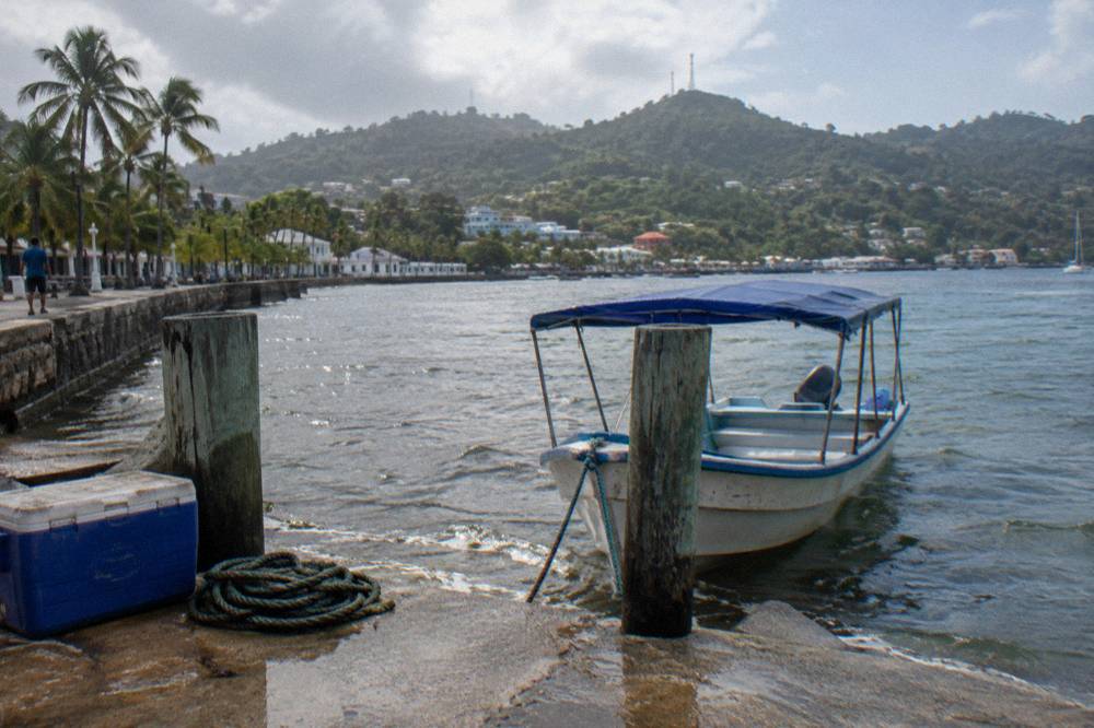 A small covered boat at a wooden dock in Samaná town with calm water beyond