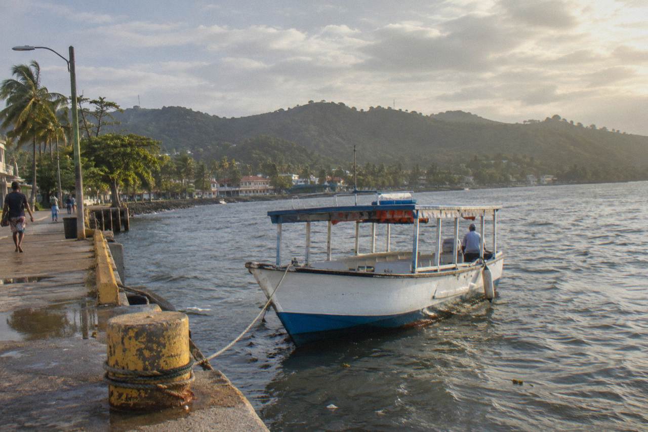 A calm bay with a small passenger boat and green hills along the shore